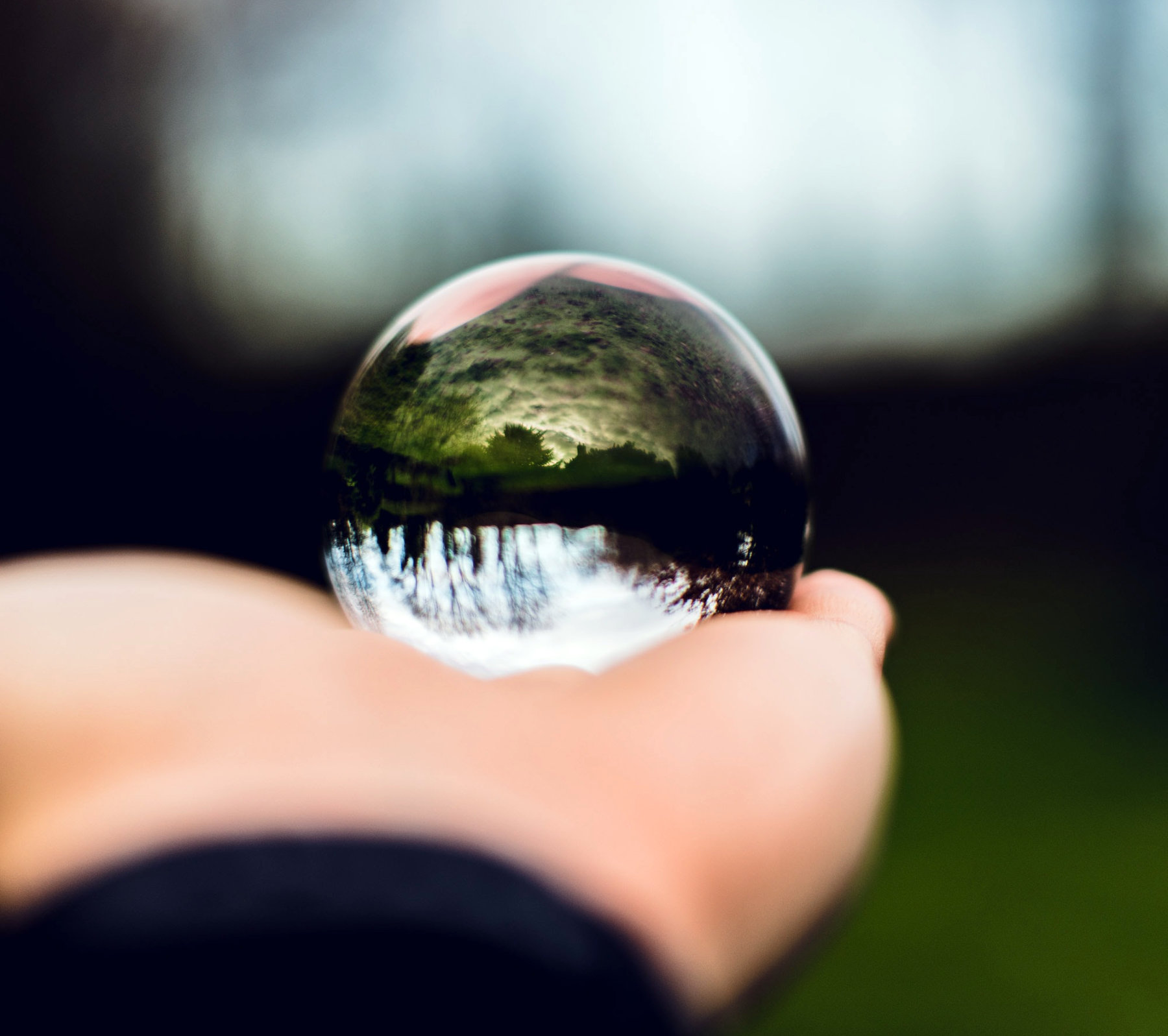 a hand holds a small glass orb reflecting the outside world